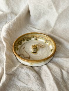 a white and gold bowl with two rings in it sitting on a cloth covered surface