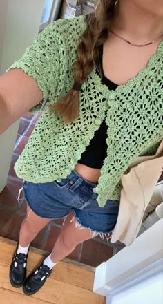 a woman is taking a selfie in the mirror with her cell phone while wearing shorts and a green crocheted sweater