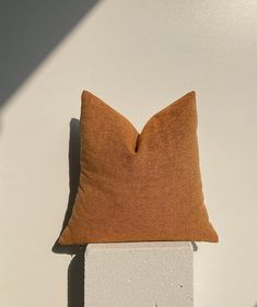 a brown pillow sitting on top of a white wall next to a cement block in the sun