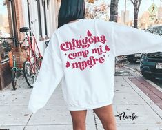 a woman is walking down the street wearing a white sweatshirt with pink writing on it