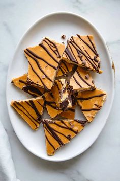 a white plate topped with pieces of chocolate and caramel swirled cheesecake bars on top of a marble counter