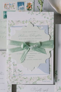 the wedding stationery is laid out on top of each other, including an envelope with a green ribbon