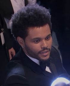 a man in a tuxedo is holding a glowing light up ball with his right hand