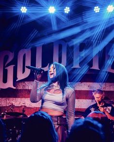 a woman singing into a microphone while standing in front of an american flag on stage