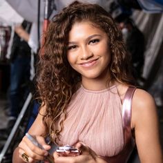 a woman in a pink dress is holding a cell phone and smiling at the camera