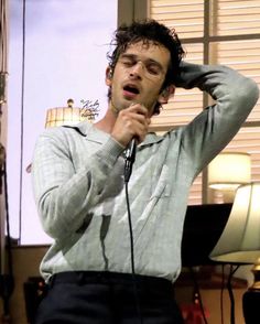 a man holding a microphone up to his ear while standing in front of a window