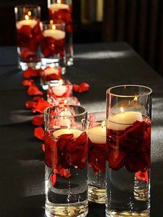 candles are lined up on a long table with red rose petals and votives