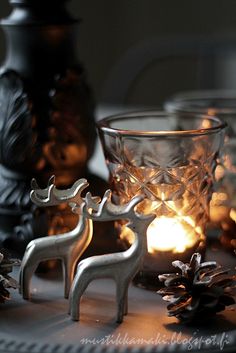 two silver deer figurines sitting on top of a table next to pine cones