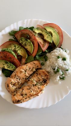 a white plate topped with chicken, rice and veggies next to sliced avocado