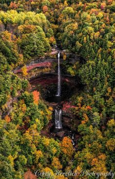 an aerial view of a waterfall surrounded by trees in the fall with colorful foliage surrounding it