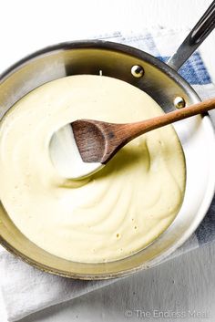 a wooden spoon in a pan filled with white sauce on top of a blue and white towel