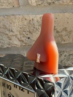 an orange ring sitting on top of a metal box next to a brick wall and clock