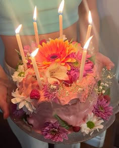 a person holding a cake with candles in it and flowers on the bottom, as if for someone's birthday