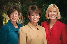 three women standing next to each other in front of trees