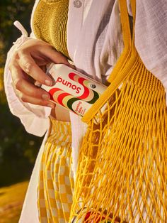 a woman holding a can of juice in her hand while wearing a yellow netted bag