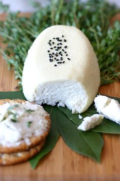 a piece of cheese with herbs on it next to some crackers and green leaves