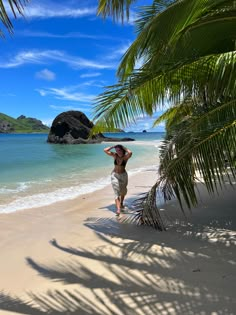 a woman walking on the beach with palm trees in front of her and an island in the background