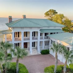 an aerial view of a large white house with palm trees and water in the background