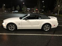 a white convertible car parked in a parking lot at night with its top down and the roof down