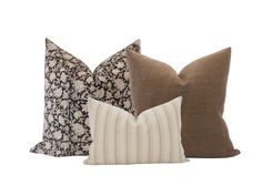 three pillows with different patterns on them, one brown and the other white are sitting next to each other