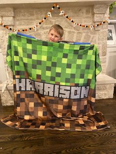 a young boy holding up a minecraft blanket in front of a fireplace with garlands