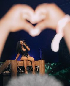 a woman sitting on top of a wooden bench with her hands in the shape of a heart