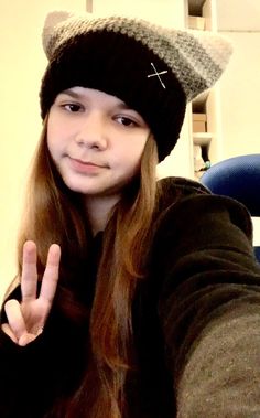 a girl with long hair wearing a hat making the peace sign