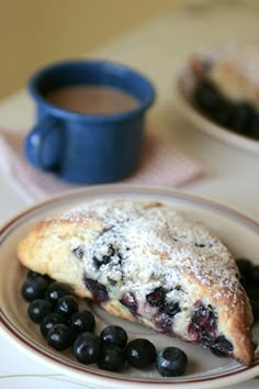 a blueberry pie on a plate next to some berries and a cup of coffee