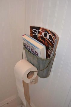 a toilet paper holder with magazines in it and a magazine on the wall next to it