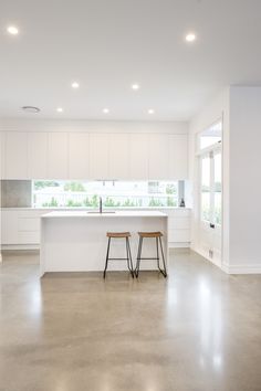 two stools sit in the middle of a large kitchen with white cabinets and counters