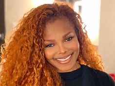 a woman with long red curly hair smiling at the camera and wearing a black t - shirt