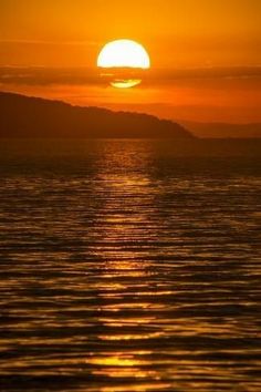 the sun setting over water with mountains in the background