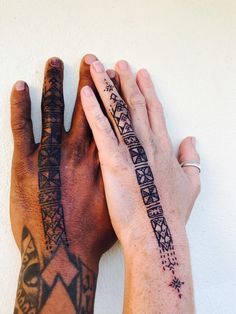 two hands holding each other with tattoos on their arms and wrist, both showing different designs