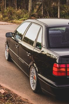 a black car is parked on the side of the road in front of some trees