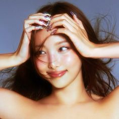 a woman with long brown hair holding her hands up to her face and looking at the camera