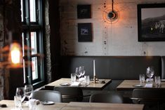 an empty restaurant with wooden tables and gray chairs in front of a brick wall that has framed pictures on it