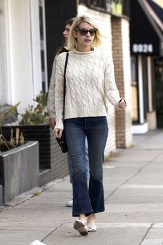 a woman in white sweater and jeans walking down the street