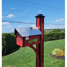 a red mailbox sitting on top of a lush green field next to a hedge