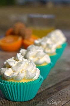 three cupcakes with white frosting sitting on top of a wooden table next to orange slices