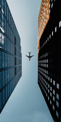 an airplane is flying in the sky between two tall buildings with windows on each side