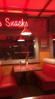 the inside of a restaurant with red neon lights and two booth seating area, along side a window that reads les snacks