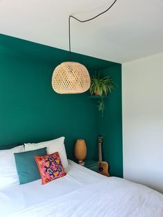 a bedroom with green walls, white bedding and a plant hanging from the ceiling