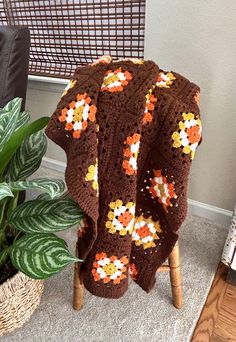 a crocheted blanket sitting on top of a wooden chair next to a potted plant