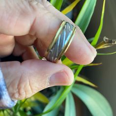 a person holding a ring in their left hand near a plant with green leaves on it