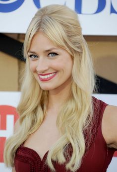 a woman with long blonde hair wearing a red dress smiles at the camera while standing in front of a sign