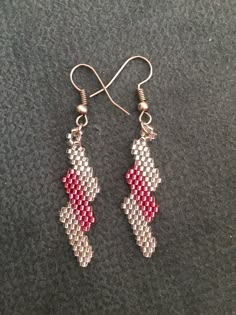 two pairs of earrings with red and white beads hanging from hooks on a gray surface