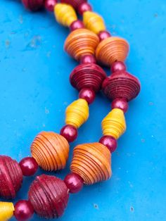 a necklace made out of red, yellow and purple beads on a blue surface with one bead in the middle