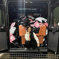 a woman is sitting in the back of a van full of bags and boxes,