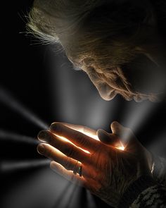 an older woman holding her hands together with light shining through the darkness in the background