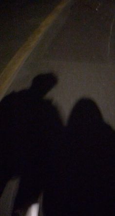 two people standing next to each other on the side of a road at night time